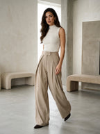 Pleated wide-leg trousers in pinstripe taupe, worn by a model in the studio