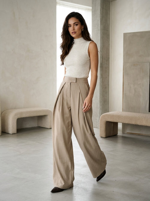 Pleated wide-leg trousers in pinstripe taupe, worn by a model in the studio