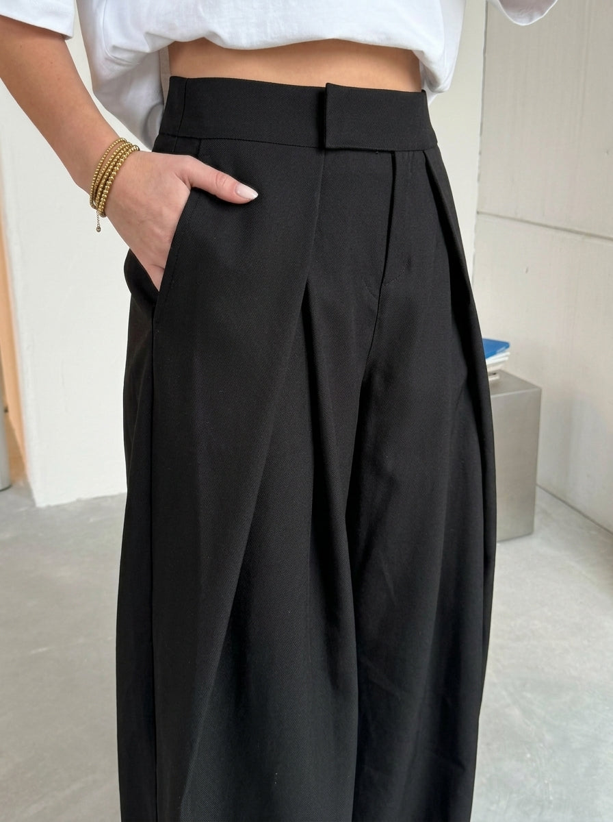 Pleated wide-leg trousers in plain black, close-up of the front pleats