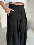 Pleated wide-leg trousers in plain black, close-up of the front pleats